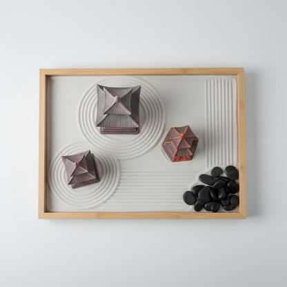 Top-down view of three japanese pagoda decor pieces arranged in a wooden zen garden tray. Raked white sand patterns surround the ceramic miniatures and a cluster of smooth black river stones, creating a peaceful atmosphere.