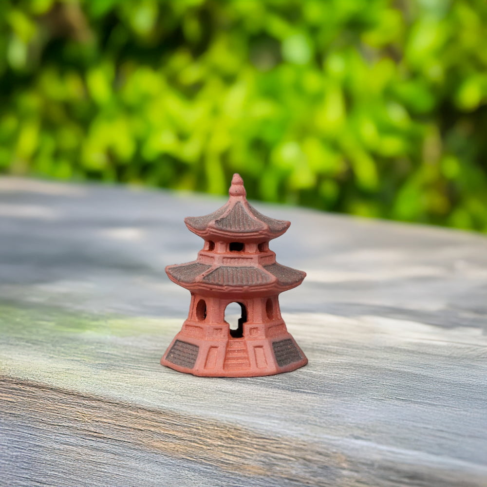 A small, red Japanese pagoda with intricate detailing stands on a textured, gray surface. The vibrant red hue of the pagoda pops against the neutral background.