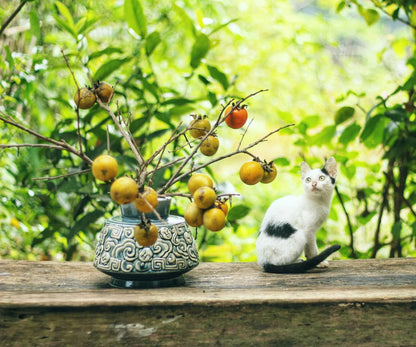  A white cat sits by a blue Vietnamese ceramic vase with a cloud motif on a wooden table. 