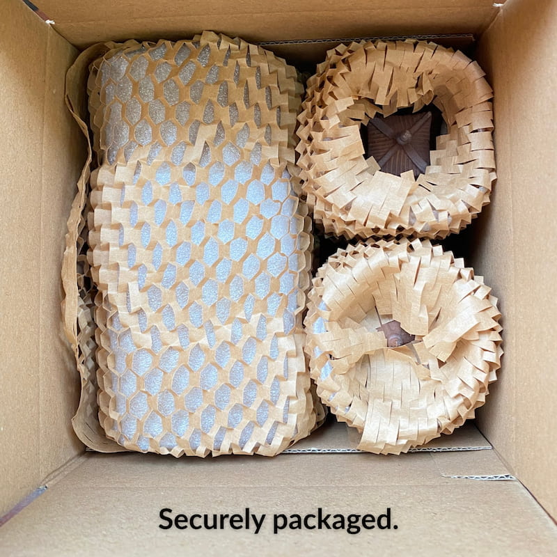 An open shipping box showing the Bat Trang ceramic pagoda figurines securely wrapped in brown protective honeycomb paper, ensuring they arrive safely.