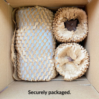 An open shipping box showing the Bat Trang ceramic pagoda figurines securely wrapped in brown protective honeycomb paper, ensuring they arrive safely.