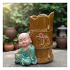  A figurine bonsai planter sits on a stone. This unique bonsai pot has a serene monk figure.