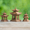 A set of three brown ceramic pagoda figurines, in different shapes and sizes, arranged on a wooden surface with a blurred green background, ready to be used as bonsai pagoda accessories.