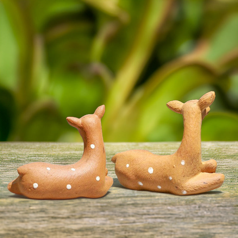 Two adorable ceramic deer, their backs turned to the viewer, gaze out over a miniature landscape, inviting you to join them in their peaceful world.