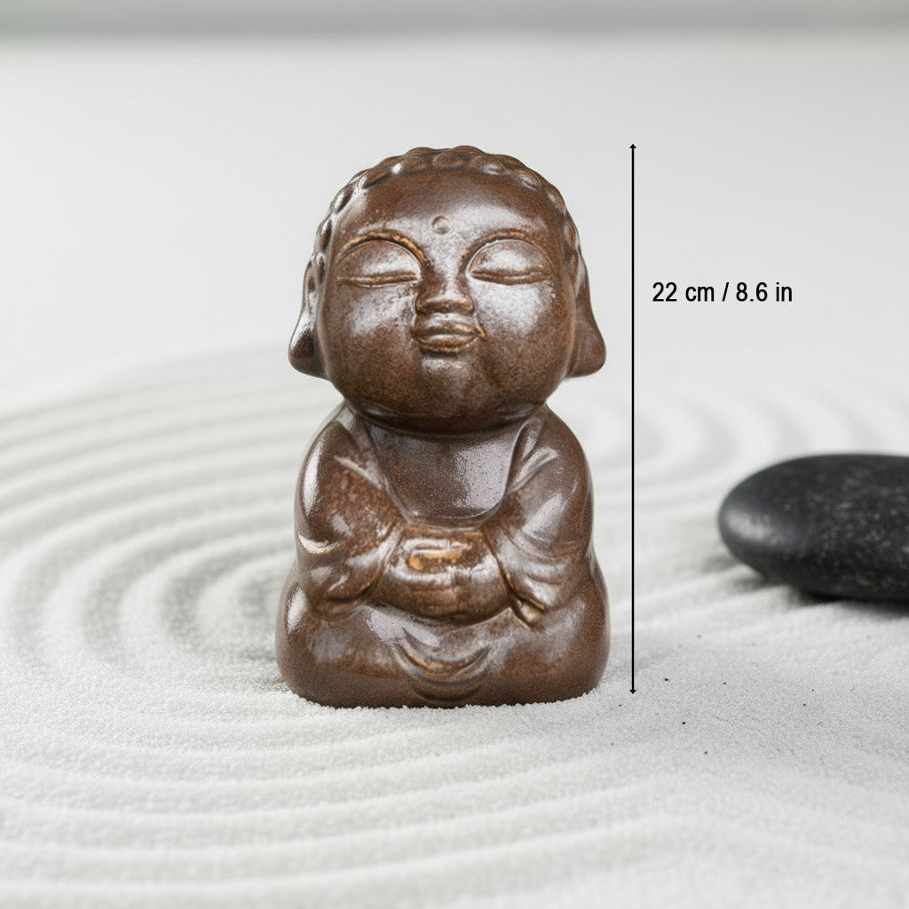 A glossy brown small buddha statue on sand. This 8.6 in ceramic buddha decor shows its size.