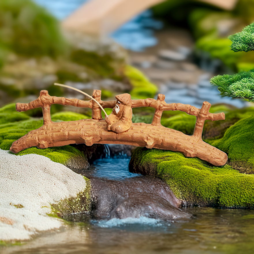 A miniature bamboo bridge with a fishing man figurine, placed over a stream in a bonsai or fairy garden setting.