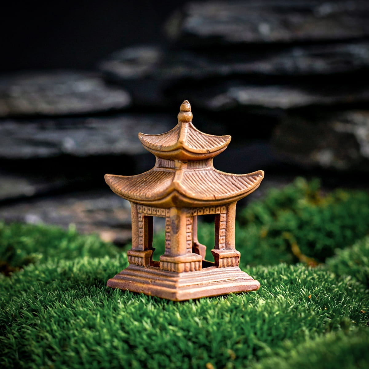 A small ceramic bonsai decor pagoda with two tiers and open pillars, placed on a bed of vibrant green moss. The earthy brown texture of the fired clay provides a serene element for Japanese decor.