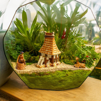 In a glass terrarium filled with lush greenery, a miniature Tam figurine sits beside a well, adding a touch of Vietnamese storytelling to this miniature ecosystem.