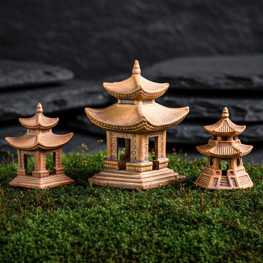 Three distinct miniature pagoda styles crafted from golden Hoang Tho clay, resting on lush green moss against a dark stone backdrop. These bonsai figurines showcase traditional Vietnamese craftsmanship and rustic texture.