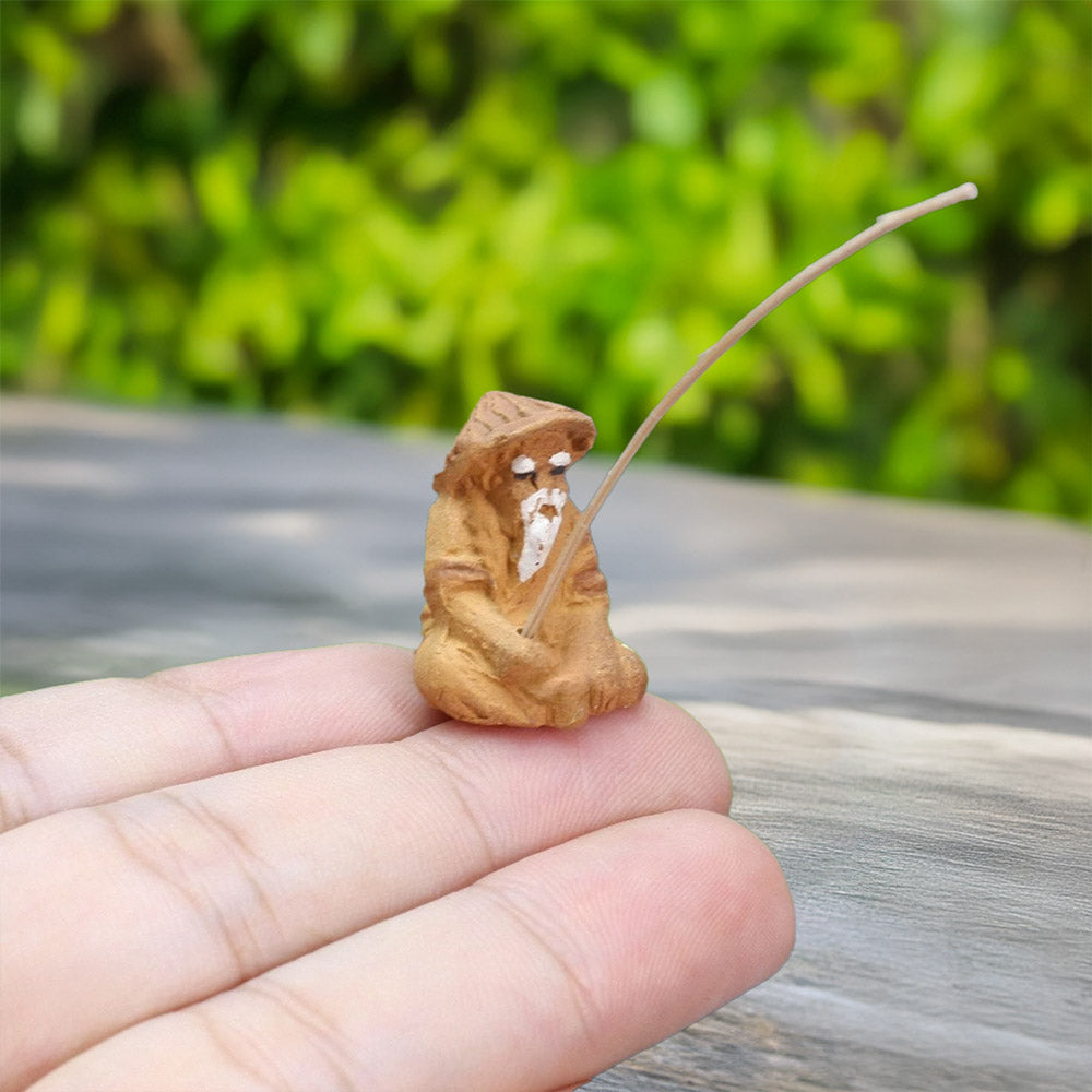 Perched delicately on a fingertip, a tiny mudman figurine, crafted from natural clay, holds his fishing rod, showcasing the intricate artistry of this miniature sculpture.