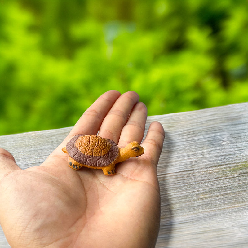 A tiny ceramic turtle, small enough to fit in the palm of your hand, is painted with earthy tones, perfect for adding a touch of whimsy to any bonsai or miniature garden.