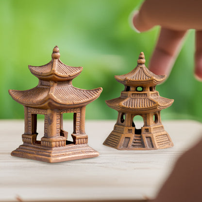 A close-up of two different miniature pagoda figurines on a wooden surface. One is a square-based ceramic pagoda figurine, and the other is a smaller, round-based Japanese pagoda statue.