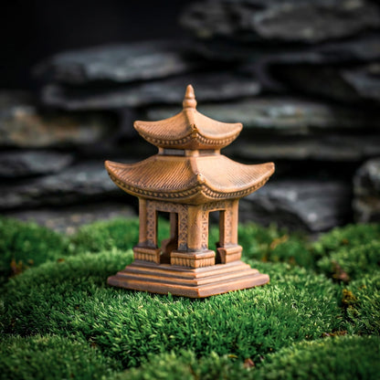 A two-tier miniature pagoda made of rustic golden clay, standing on a mossy surface. The detailed roof tiles and open structure make it an ideal bonsai decor pagoda for outdoor or indoor use.