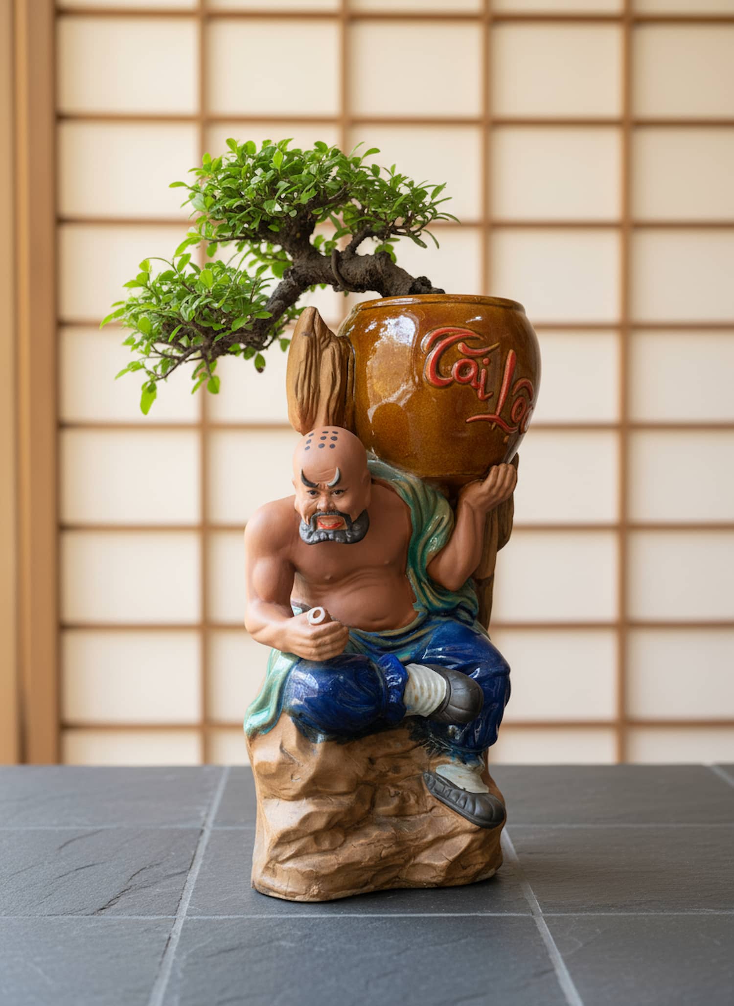 A man figurine holds a pot with a bonsai. This unique bonsai pot is a great statue bonsai planter.