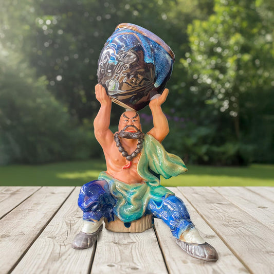 The empty statue bonsai planter is a strong man holding a dark blue glazed pot.