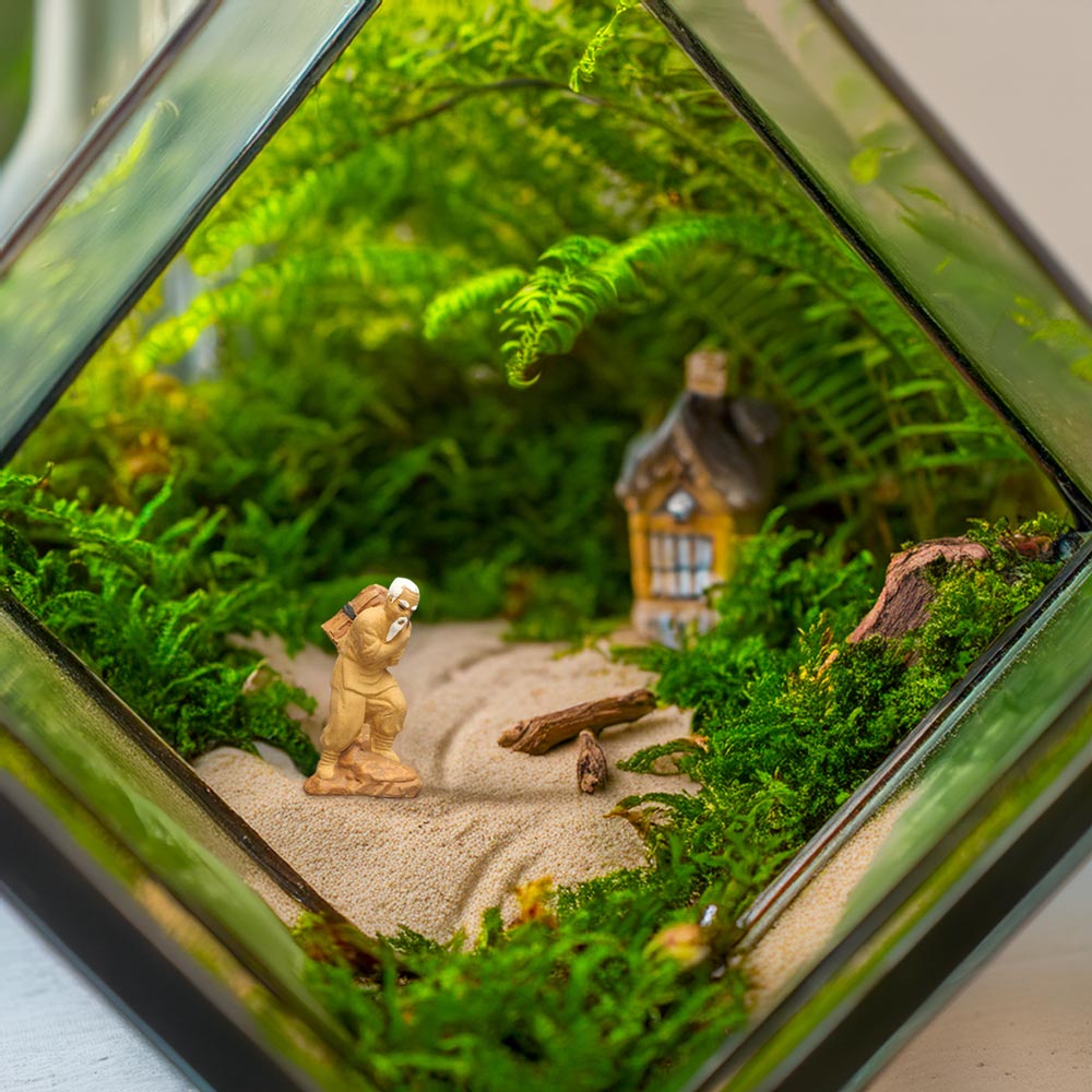 A miniature woodcutter terrarium figurine is walking on a sand path through a terrarium filled with green moss and ferns.