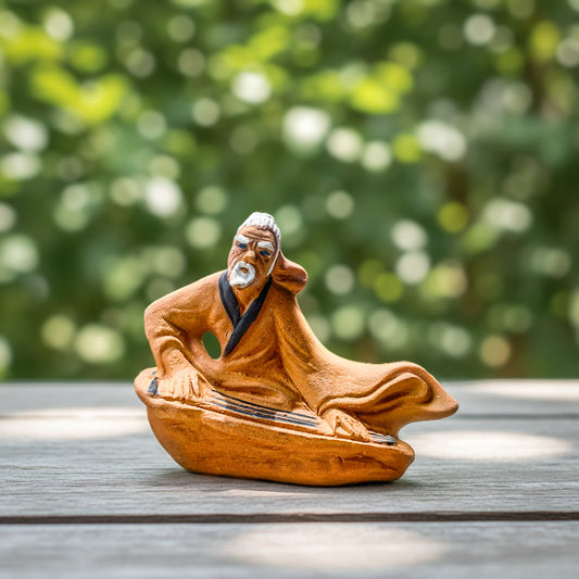 Zither Player Mudman Ceramic Figurine on a wooden surface with a blurred green background.