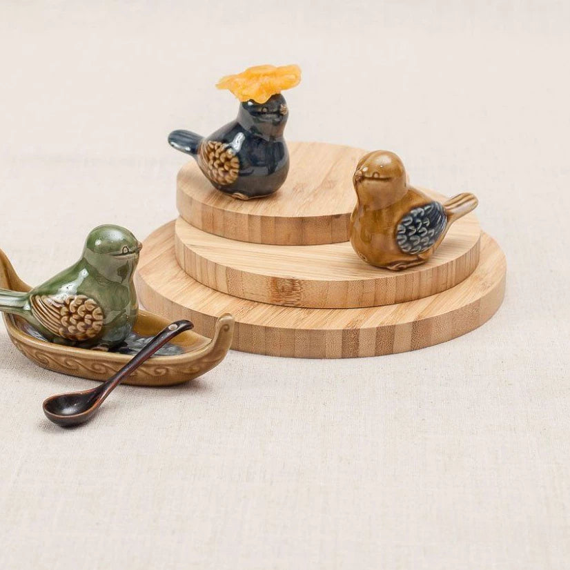 Three Vietnamese ceramic bird figurines in green, blue and yellow glazes, with one resting on a boat-shaped ceramic dish