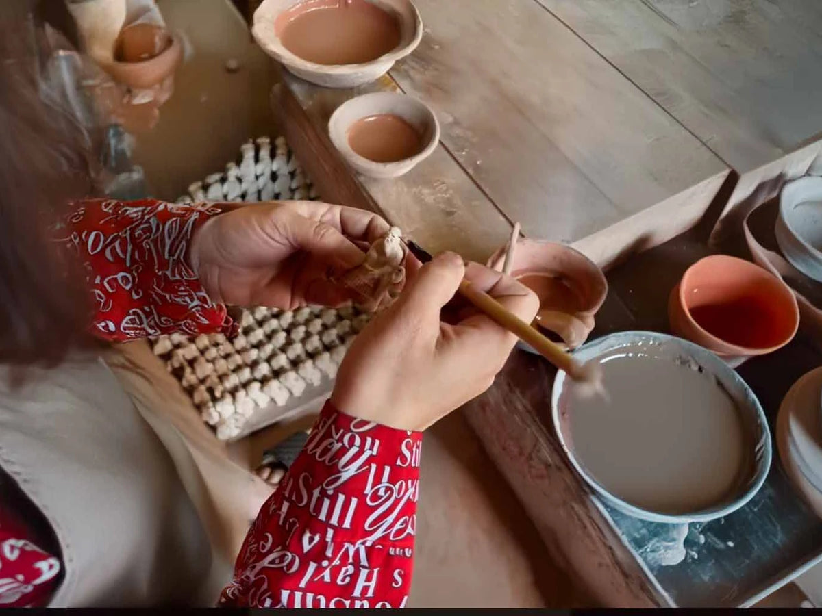 Hands applying glaze to small ceramic figurines with a brush at Duc Huy Pottery.